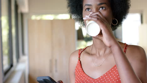 african american casual businesswoman drinking coffee and using smartphone in office, slow motion