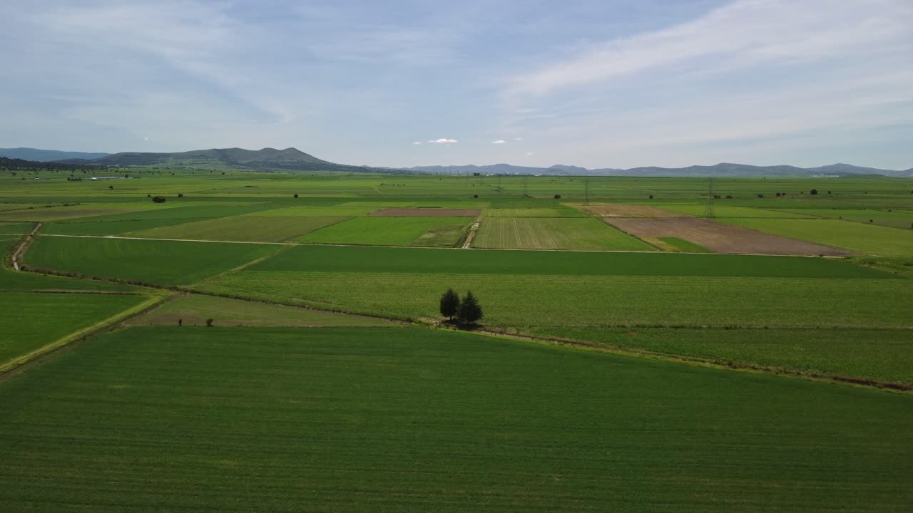 In Tlaxcala, Mexico, which is surrounded by beautiful vegetation and has Popocatepetl volcano in the distance, there is a view of agricultural fields