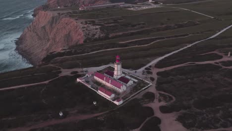 tilt up shot of rocky coast and ocean view around cabo espichel lighthouse in portugal, aerial