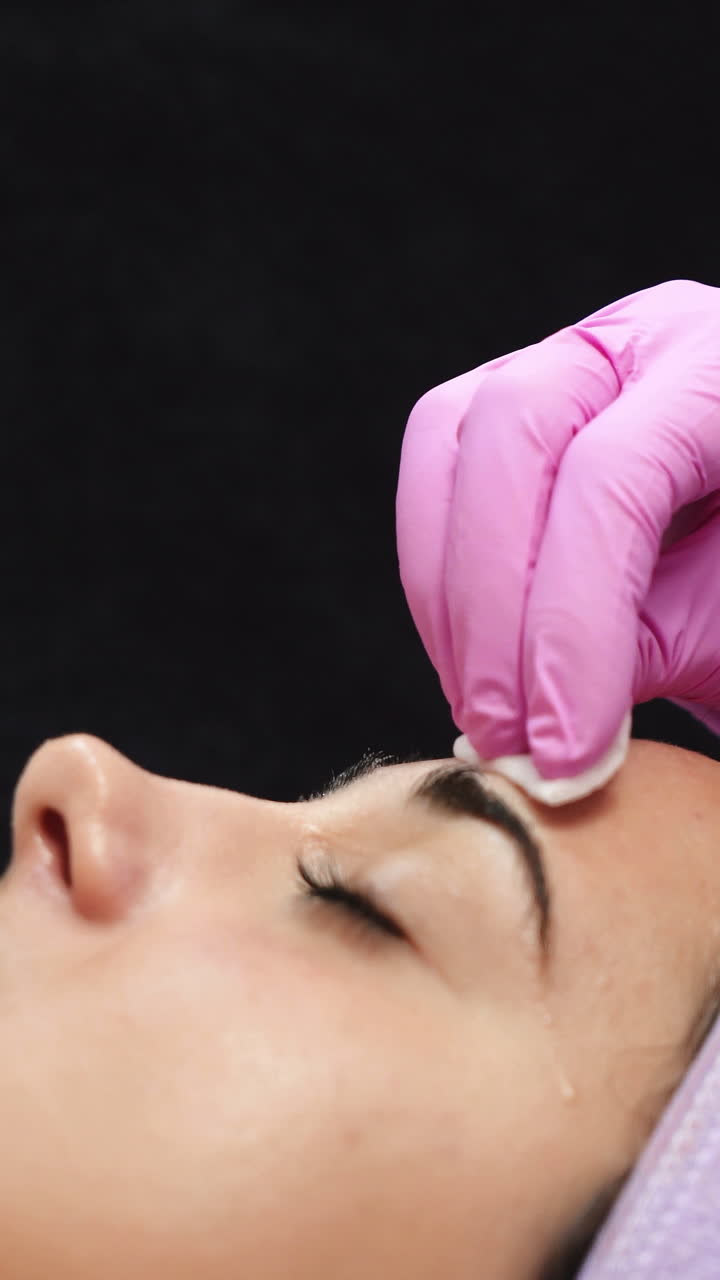 Female cosmetologist using ultrasonic scrubber on client's face. Professional ultrasonic equipment. Vertical video