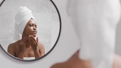 Happy-african-american-woman-apply-cream-on-face-in-bathroom