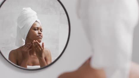 feliz mujer afroamericana aplica crema en la cara en el baño
