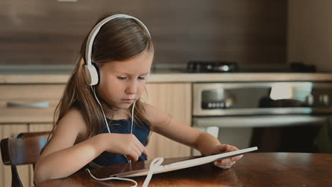 little girl with headphones uses tablet at home