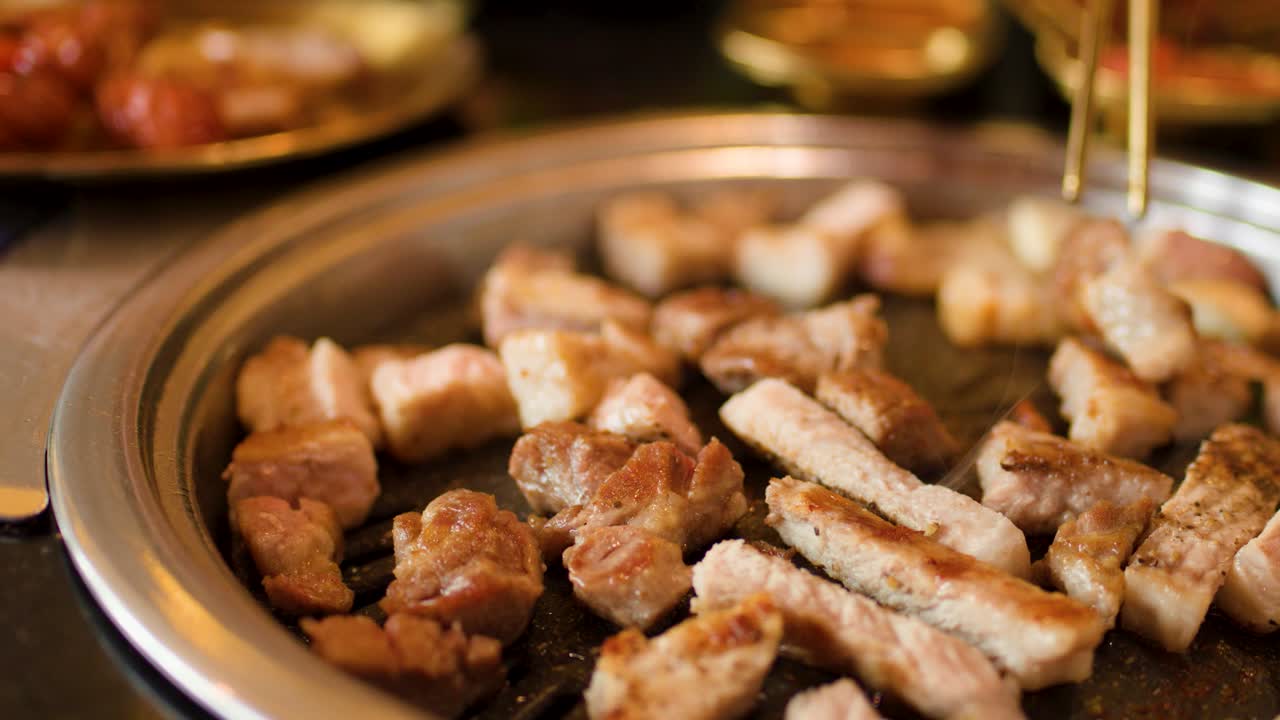 Sliced pork belly and vegetables cook on a round grill, warm lighting, close-up perspective