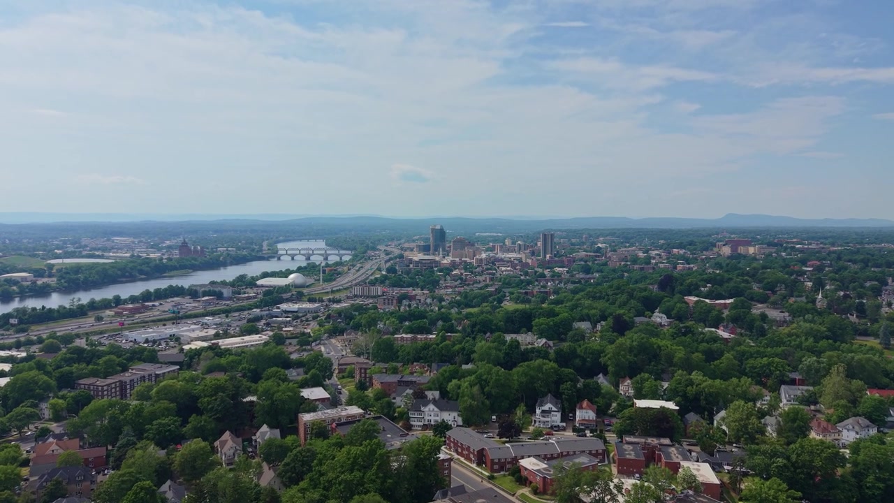 Toma aérea cinematográfica que muestra el extenso paisaje urbano de Springfield, Massachusetts, con el pintoresco río Connecticut y exuberantes árboles verdes