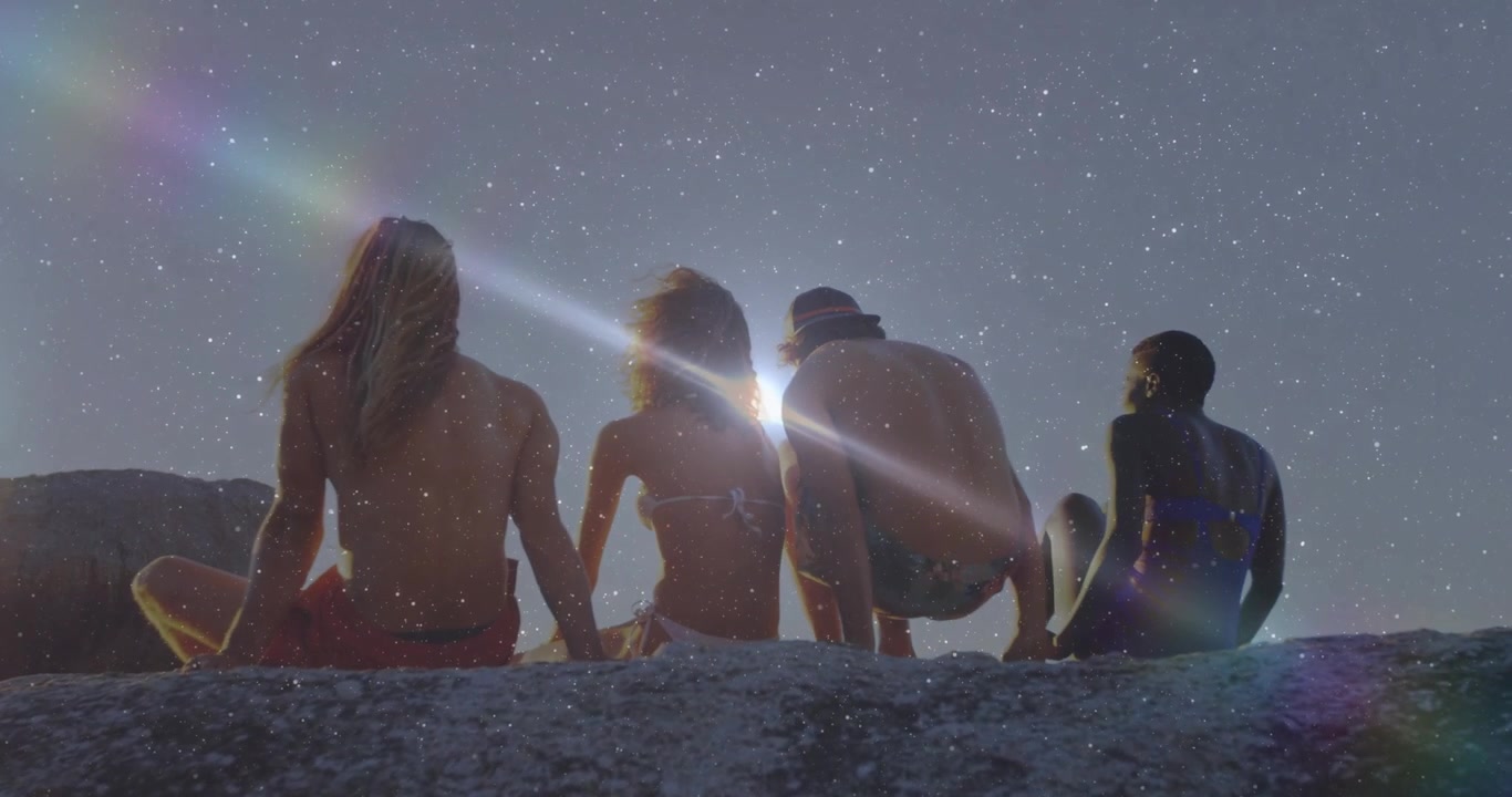 Sol se pondo no horizonte, com amigos se ajeitando em uma saliência rochosa, criando um reflexo de lente para um anúncio de viagem.
