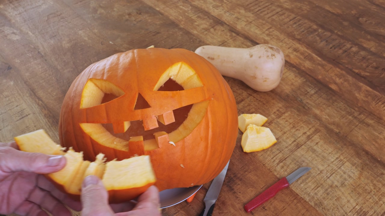 A man pulls out a cut-out mouth part from a pumpkin to create a lantern with triangular eyes, a nose and a laughing mouth.