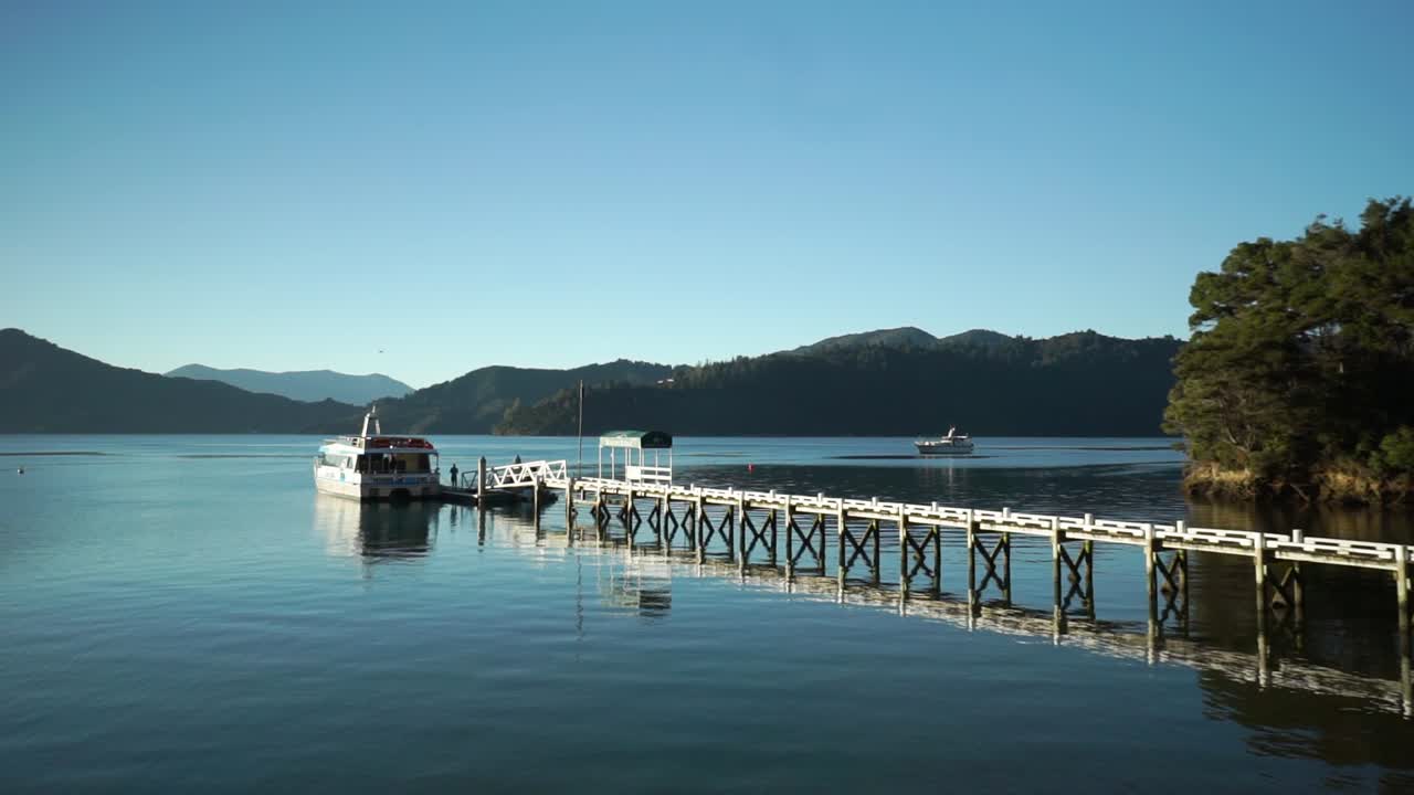 이른 아침 동안 작은 보트와 산을 배경으로 뉴질랜드 말버러 사운드에 있는 고급 별장 옆에 있는 크루즈 관광 투어 보트