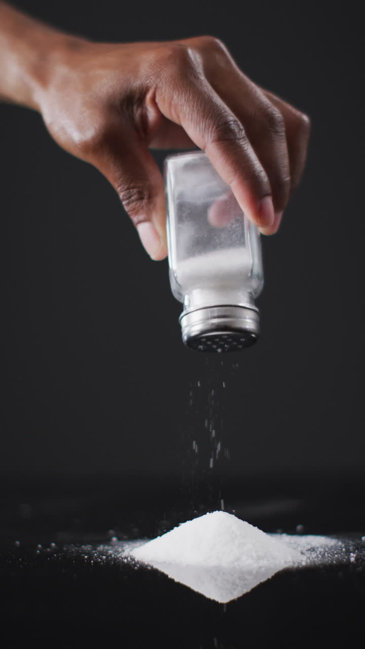 아프리카계 미국인 남자의 손이 지하실에서 검은색 표면의 어리로 소금을 흔들고 있는 수직 비디오