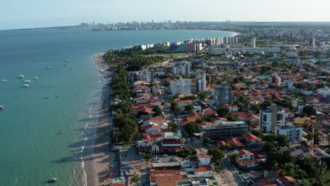 incline hacia arriba un dron aéreo en ascenso toma extrema de la playa tropical bessa en la ciudad de joao pessoa, paraiba, brasil con gente disfrutando del océano, botes turísticos y un gran paisaje urbano en el fondo