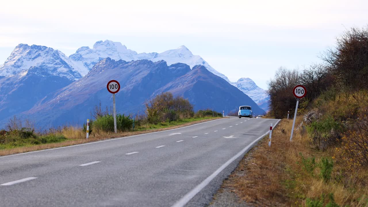 A car travels along a winding road with stunning mountain views in Glenorchy, New Zealand. Clear skies and natural beauty abound