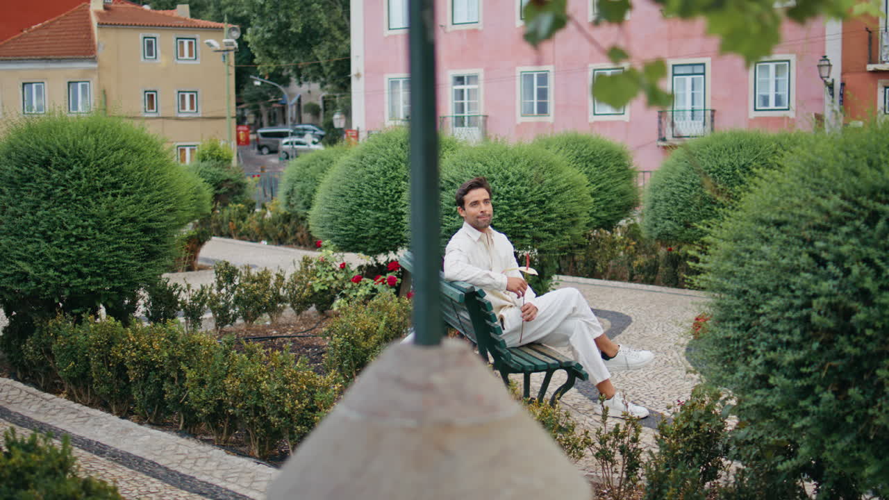 hombre romántico esperando a su novia en el banco del parque verde. novio con una flor