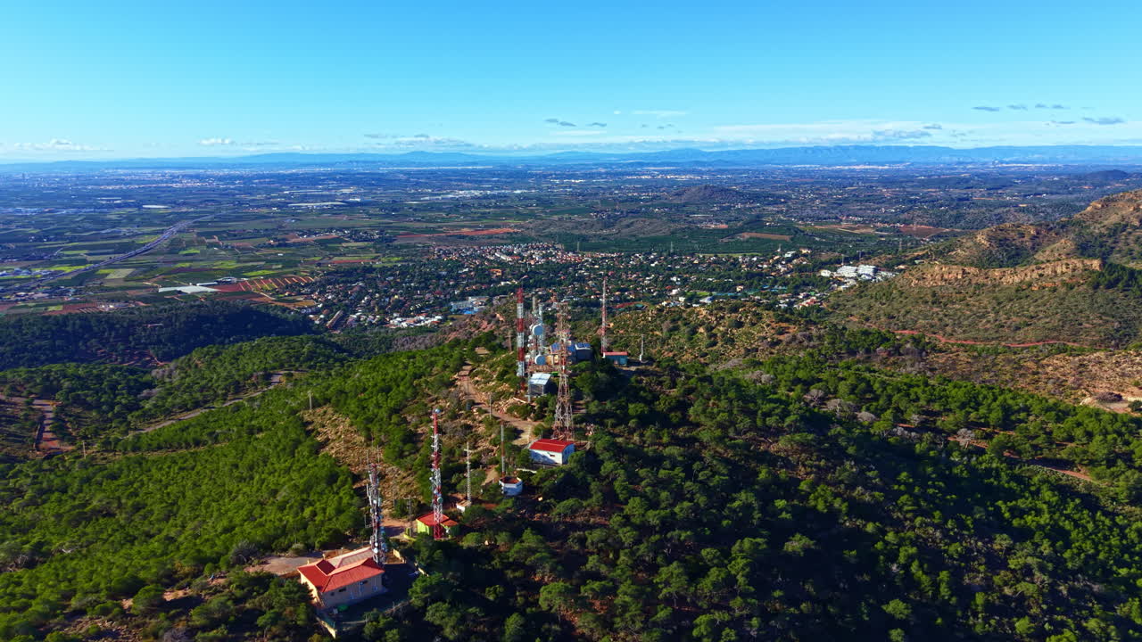 Ampia vista di torri di comunicazione e paesaggio verde di giorno, vicino a una città, con colline e campi sullo sfondo sotto un cielo azzurro e limpido.