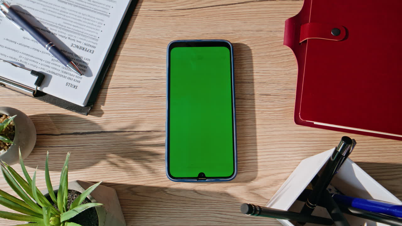 Fingers scrolling greenscreen mobile phone on desk with work tools closeup