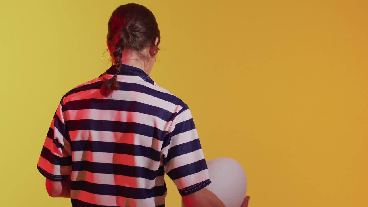 Jogadora de rugby caucasiana com bola de rugby sob iluminação amarela neon