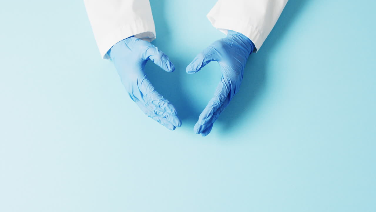 video de las manos del médico en guantes quirúrgicos haciendo forma de corazón sobre fondo azul con espacio de copia