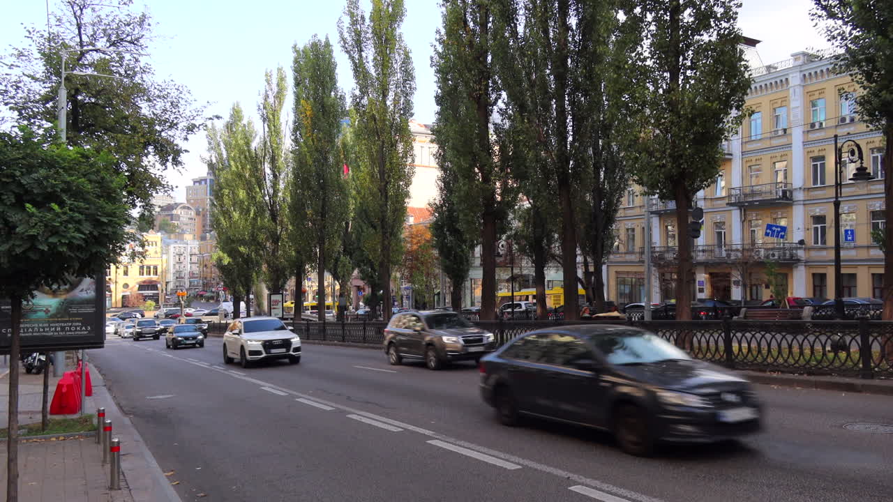 Busy street with tall trees and many cars driving in Kyiv city center Ukraine, area near Khreshchatyk Street, 4K static shot