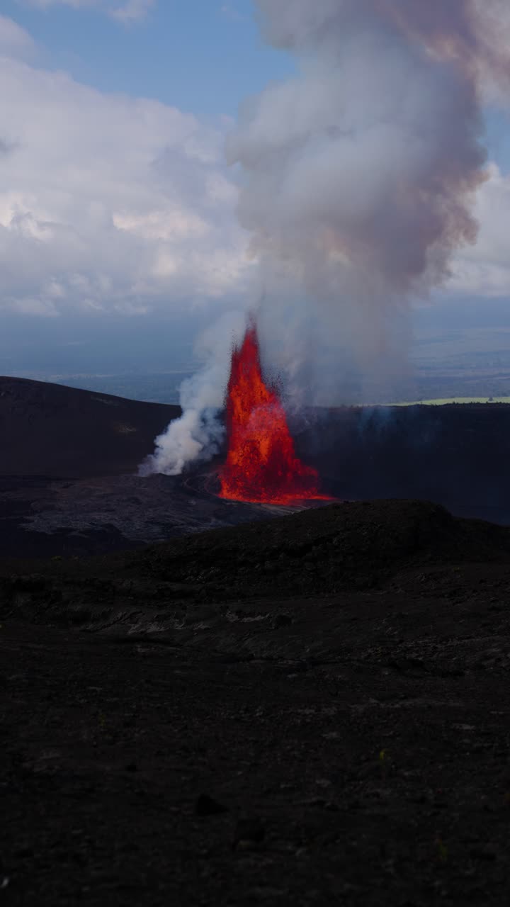 Vista verticale al rallentatore dell'eruzione del vulcano Kīlauea a Big Island, Hawaii, con vivida esplosione di lava e densa nuvola di cenere sopra un terreno di basalto scuro