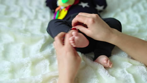 mother takes her baby's little feet in her arms. child lying on bed with a toy in his hands in blur. white backdrop.