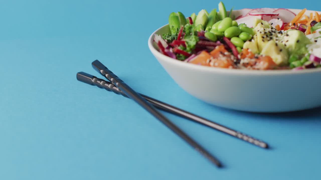 Composition of bowl of rice and vegetables with chopsticks on blue background