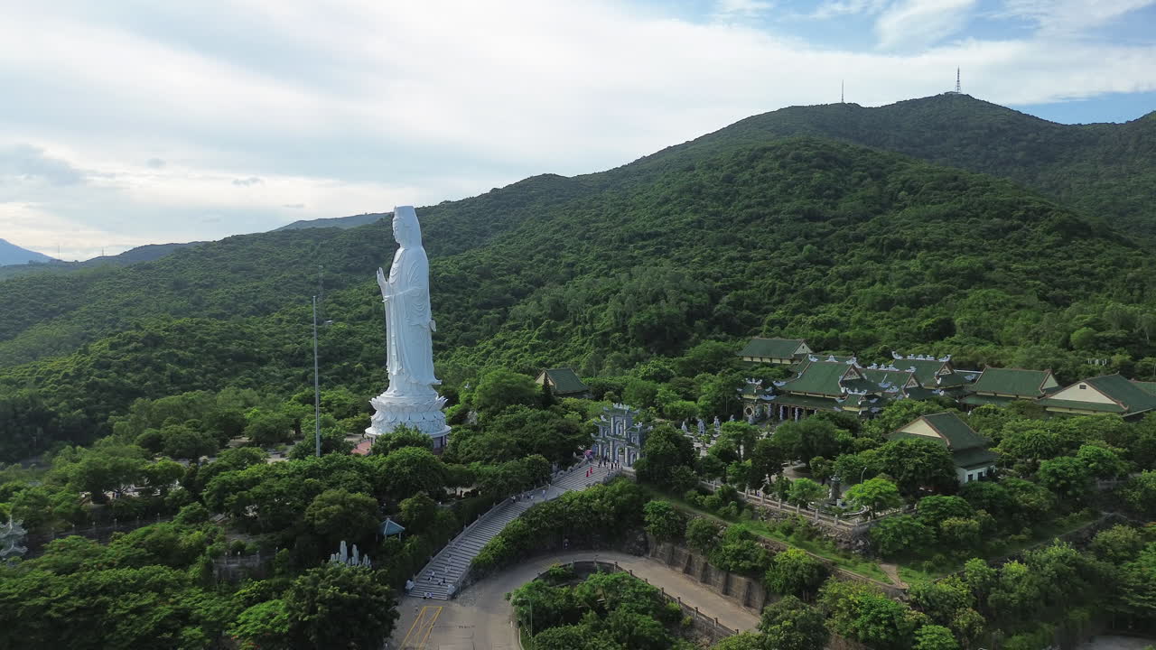 Massive Lady Buddha statue overlooking coastline in Da Nang, Vietnam, lush hills, aerial pullback