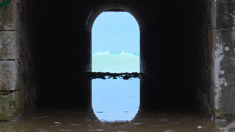 tunnel leads way to a wild sea, where crashing waves rush in and create a rippling effect