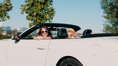 dos mujeres disfrutando de un viaje por carretera en un coche convertible