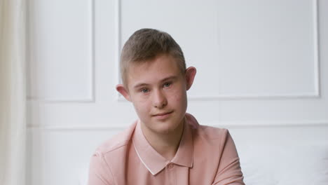 boy with down syndrome smiling at camera sitting on the bed in the bedroom at home