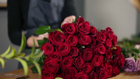 perfect bunch of red roses on the table. close up view of hands of female florist arranging modern bouquet using beautiful red