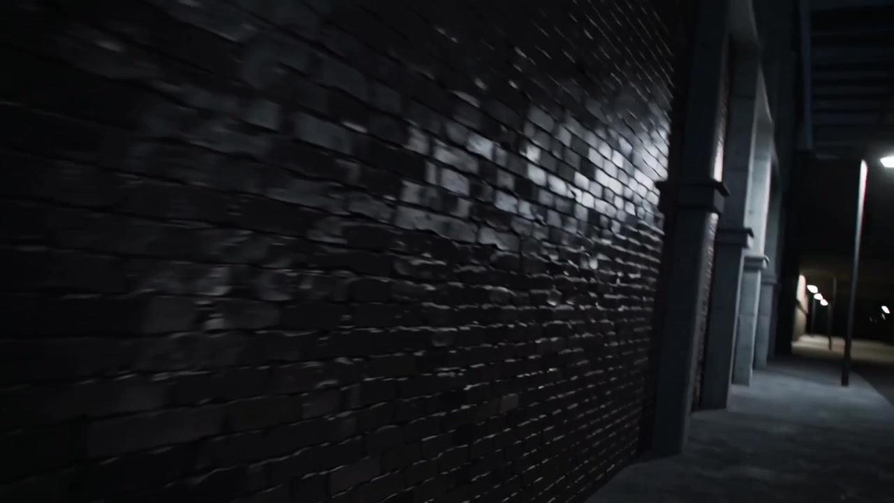 Un triangolo scuro scorre tagliando una superficie ruvida, la telecamera si allontana rivelando un sottopassaggio con muro di mattoni bagnato.