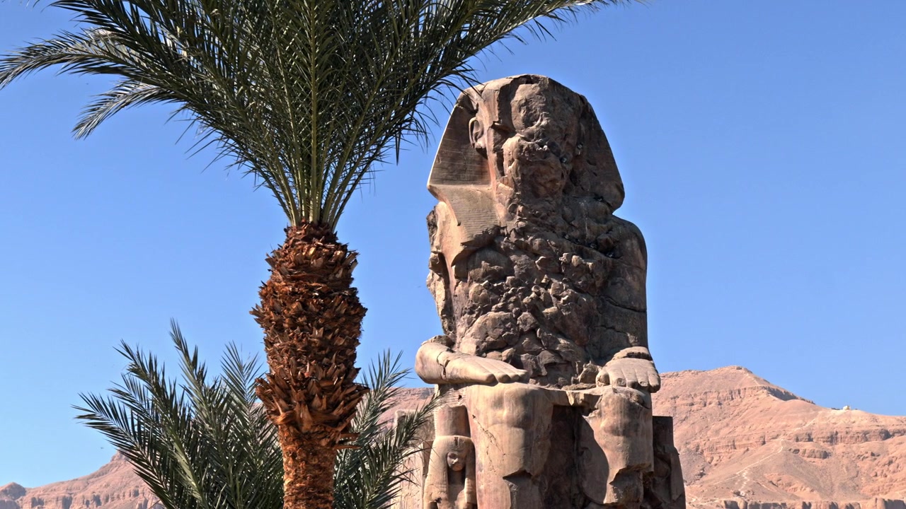 Záběr z úrovně očí zachycující jednu ze dvou masivních soch z křemencového pískovce, známých jako Memnonovy kolosy v Luxoru, Egypt