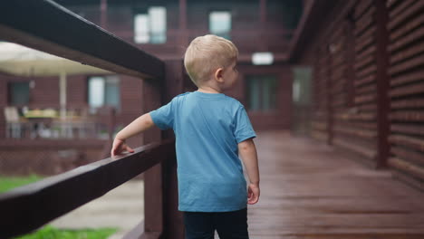 sweet boy walks holding handrail along wet veranda deck