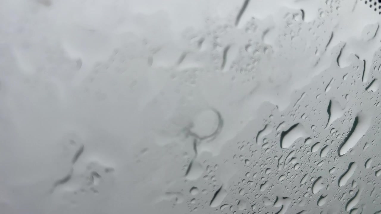 Nahaufnahme von Wassertropfen, die während eines Regensturms an einer Glasoberfläche heruntergleiten. Ideal für stimmungsvolle Hintergründe, Wetterberichte und filmische Übergänge