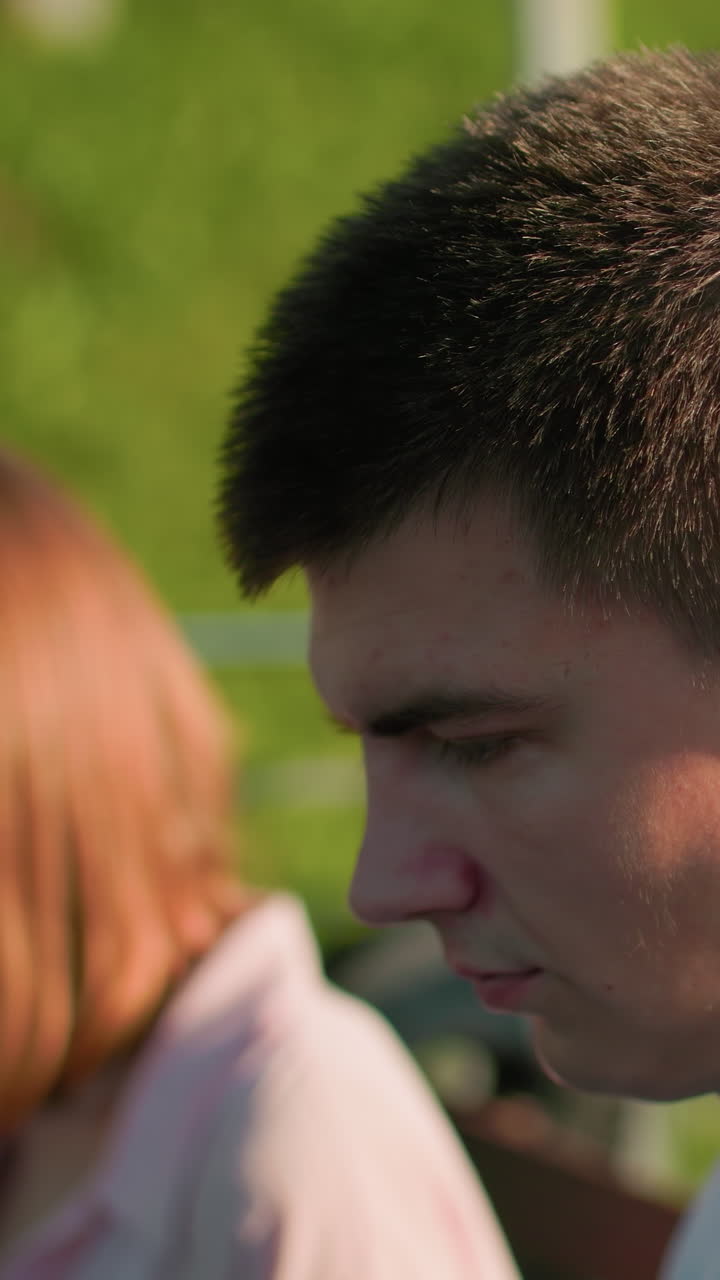 el hombre en foco mira a la mujer a su lado, el fondo borroso destaca su interacción, con árboles y barandillas de hierro que mejoran el fondo verde de la colina