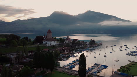 vista aérea acercándose al castillo schloss spiez en la orilla del lago thun después del atardecer