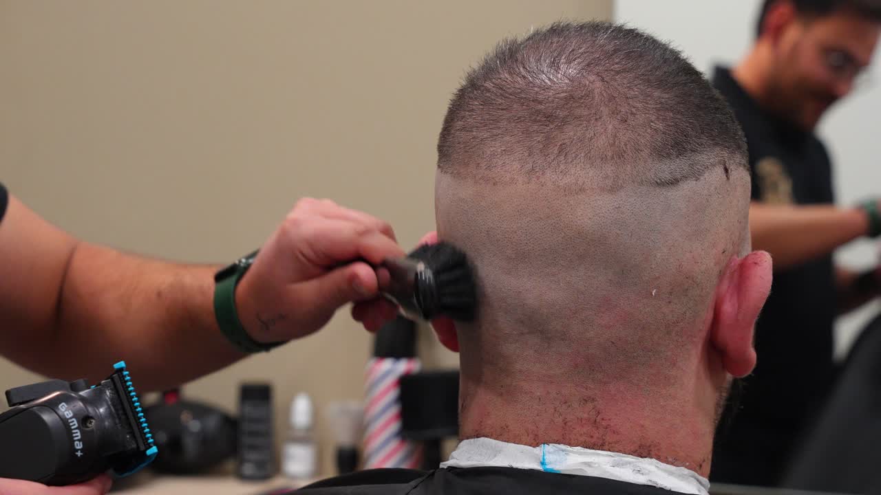 Hairdresser trims upper part of customer's head with trimmer after shaving the lower section in barbershop