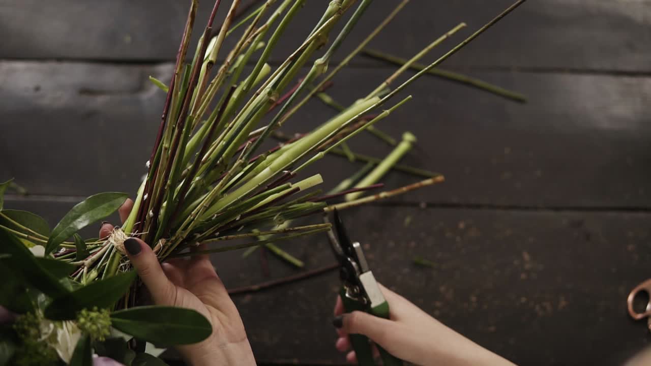Beautiful female hands cut the stems of flowers with a pruner on a dark surface. Floral studio. Top shot