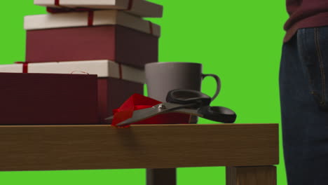 close up of man putting present into gift wrapped box on table shot against green screen 2