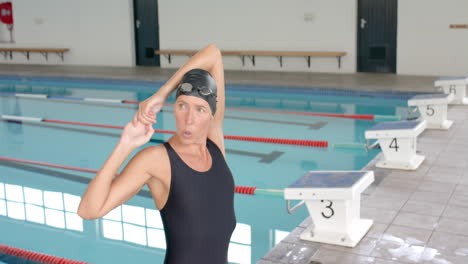 caucasian female swimmer athlete adjusts her swimming cap poolside