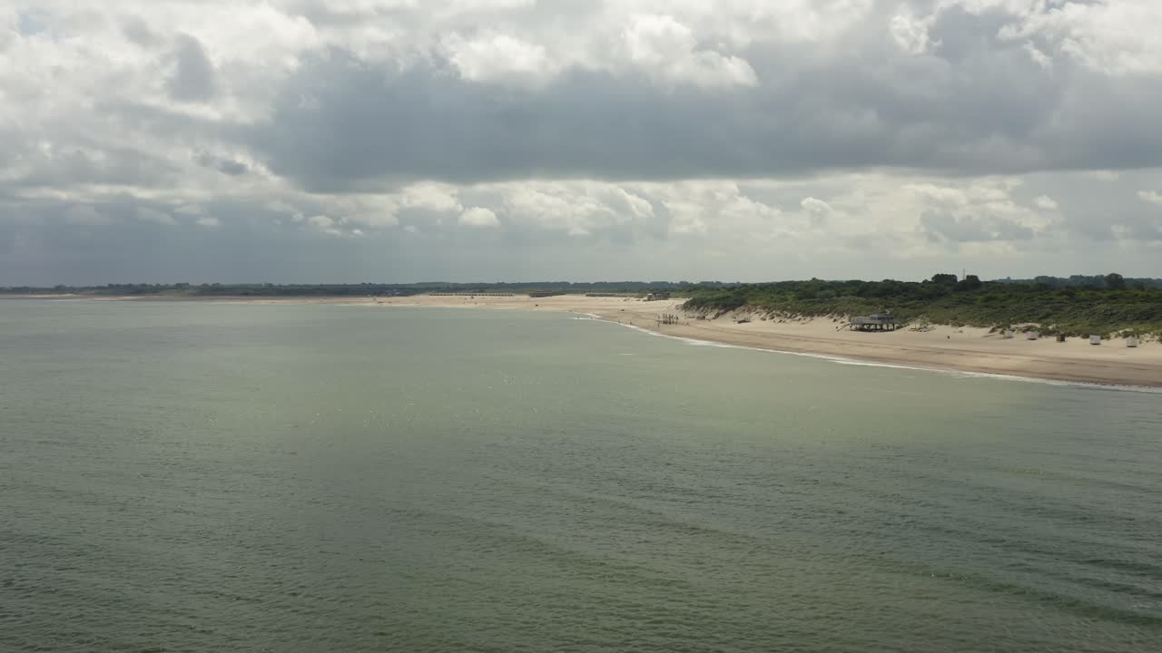 Long aerial shot of a coastline with a beach and green dunes in Zeeland, the Netherlands, on a cloudy day