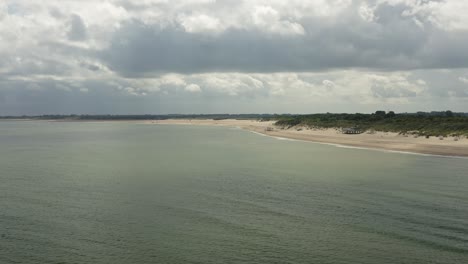 Toma-Aérea-Larga-De-Una-Costa-Con-Una-Playa-Y-Dunas-Verdes-En-Zelanda,-Los-Países-Bajos,-En-Un-Día-Nublado