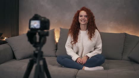 atractiva joven pelirroja rizada vlogger está hablando frente a la cámara grabando video para blog en línea en internet hablando, sonriendo y gestando. la mujer lleva vaqueros y suéter blanco. video acelerado