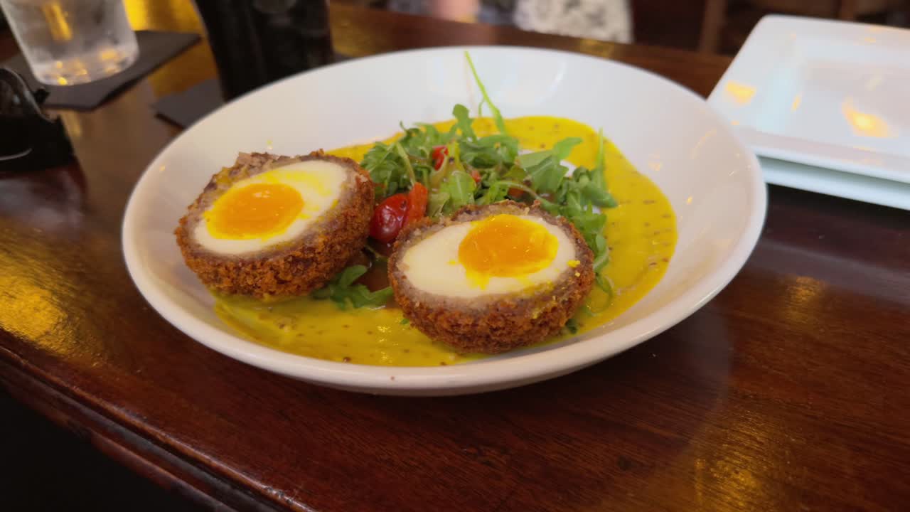 Scottish Egg and salad in a mustard sauce in a white dish.