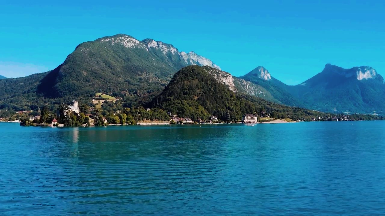 Annecy Gölü'ne uzanan yemyeşil bir yarımadada zarifçe duran tarihi ortaçağ Duingt Şatosu'nu ortaya çıkarmak için görkemli dağ sırtlarının üzerinden geçen nefes kesici sinematik bir hava görüntüsü.