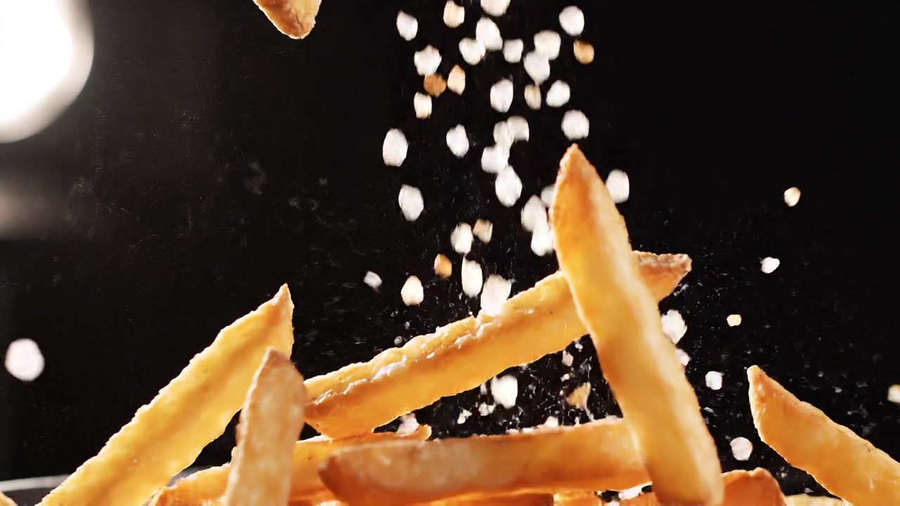 Golden Crispy French Fries Falling Against Black Background with Salt