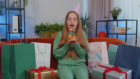 happy young teen girl celebrating birthday party, makes wish blowing burning candle on small cupcake