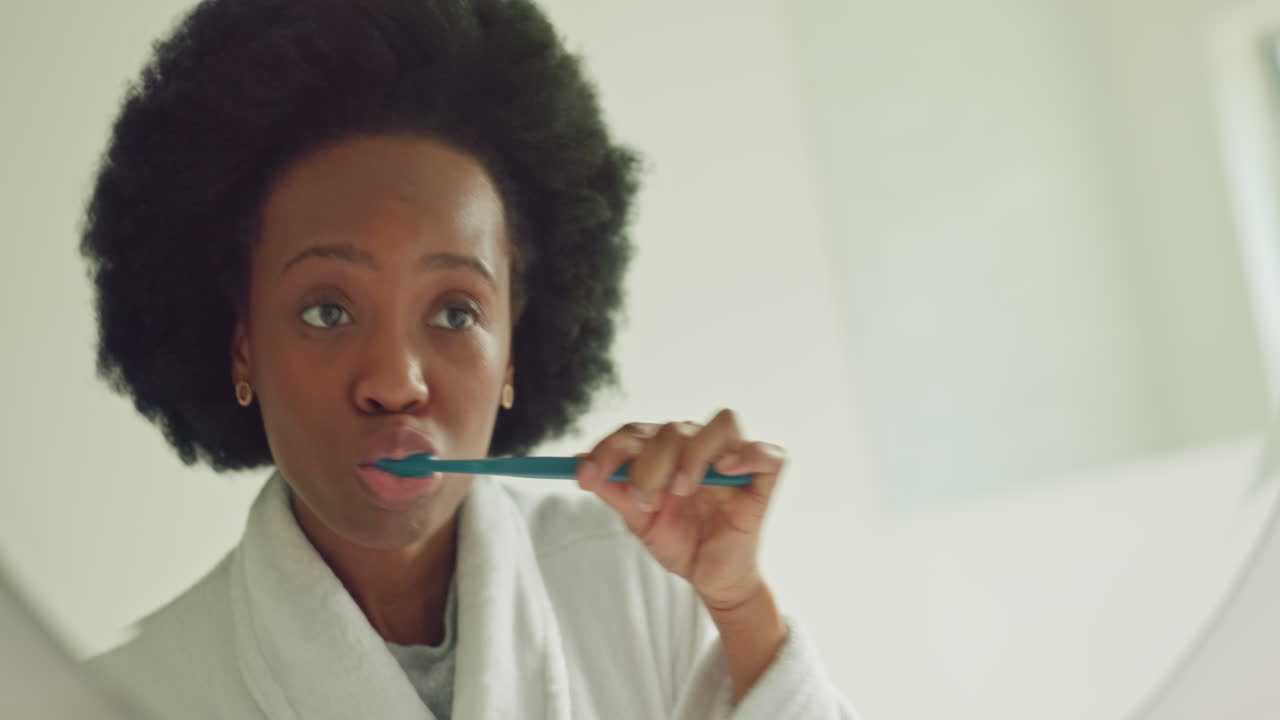 Black woman brushing teeth in bathroom mirror