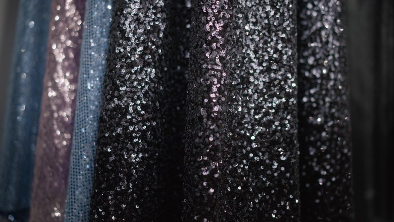 Primo piano di tessuto di vestito nero con paillettes, con texture scintillante e illuminazione soffusa. Il materiale del vestito mostra dettagli scintillanti appesi verticalmente in un ambiente di vendita al dettaglio di moda. Lo sfondo include