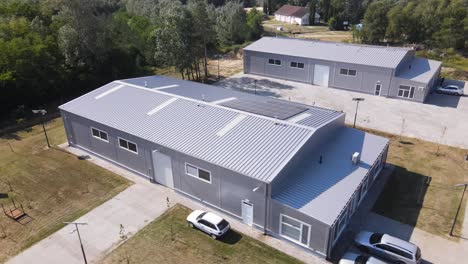 aerial drone orbital shot of a building with solar panels on the roof and solar panels on poles around the building, tompa, hungary