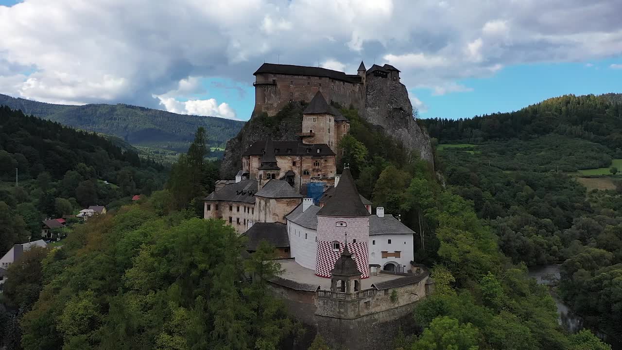 Circling Orava Castle from above, a drone captures the sweeping views of ancient fortifications surrounded by vibrant forests and dramatic hills